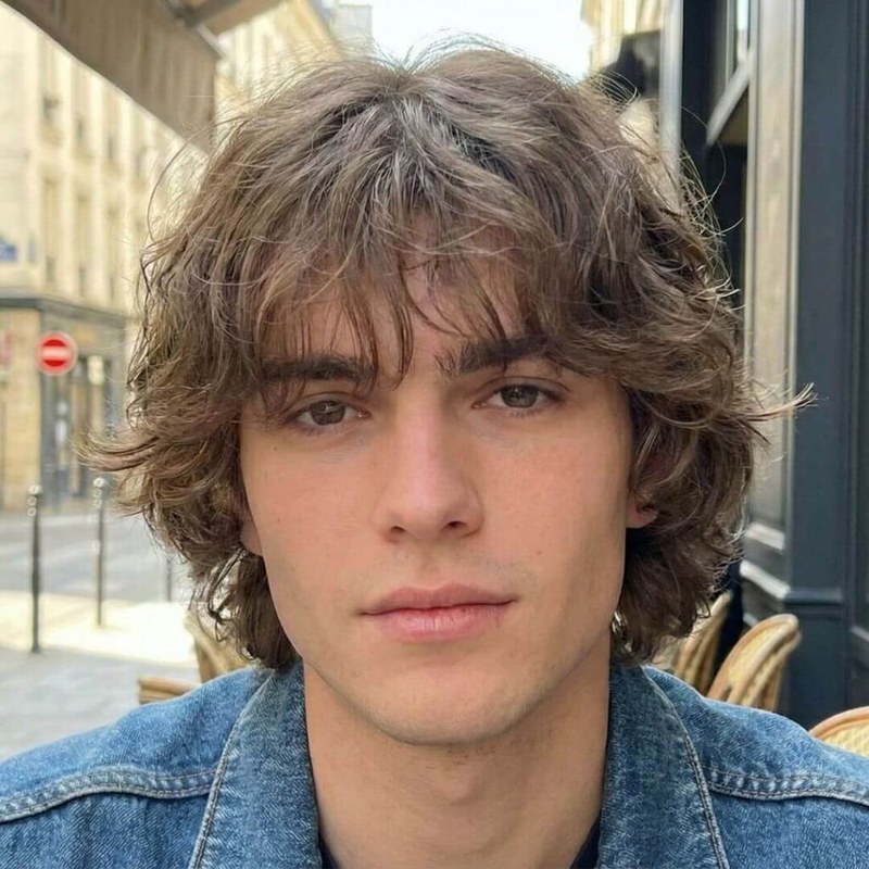 Man with wavy, medium-length blonde hair, low fade, and textured, tousled layers