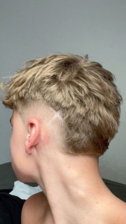 Blonde textured top over darker sides with a high-contrast rounded burst fade behind the ear
